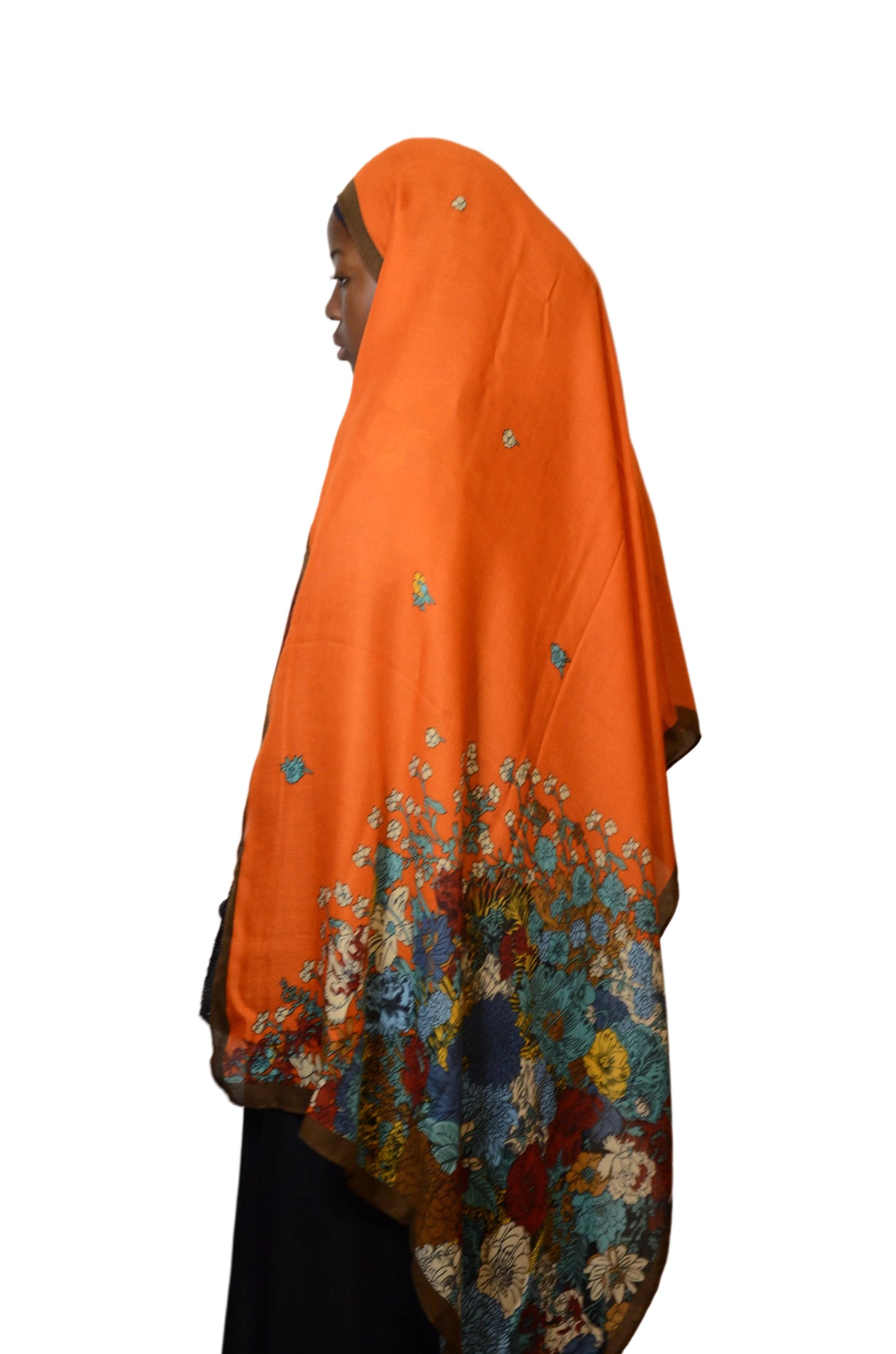 Model wearing a burnt orange cotton voile linen hijab with multicolour floral border, shown from side view with flowing drape.