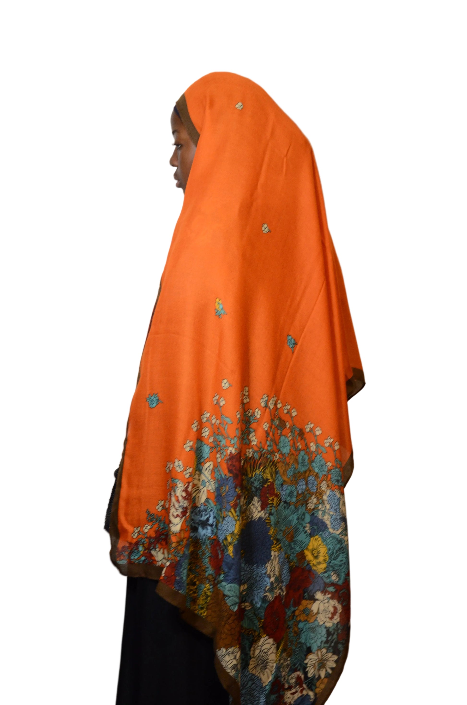 Model wearing a burnt orange cotton voile linen hijab with multicolour floral border, shown from side view with flowing drape.