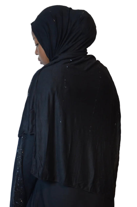 Model wearing a black plain jersey hijab with subtle black bead detailing styled over a black abaya.