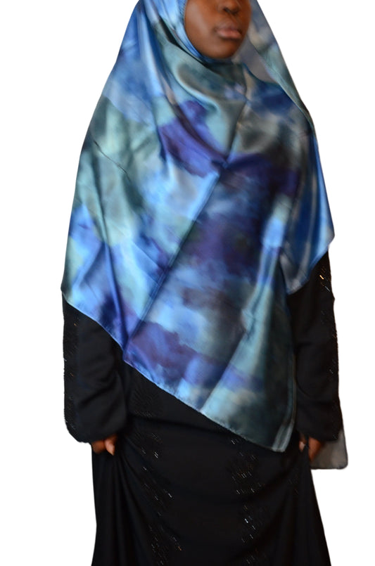 Model wearing a blue marble satin-feel hijab with fluid drape, shown from the side and back, featuring deep navy and teal tones with an abstract watercolor pattern.