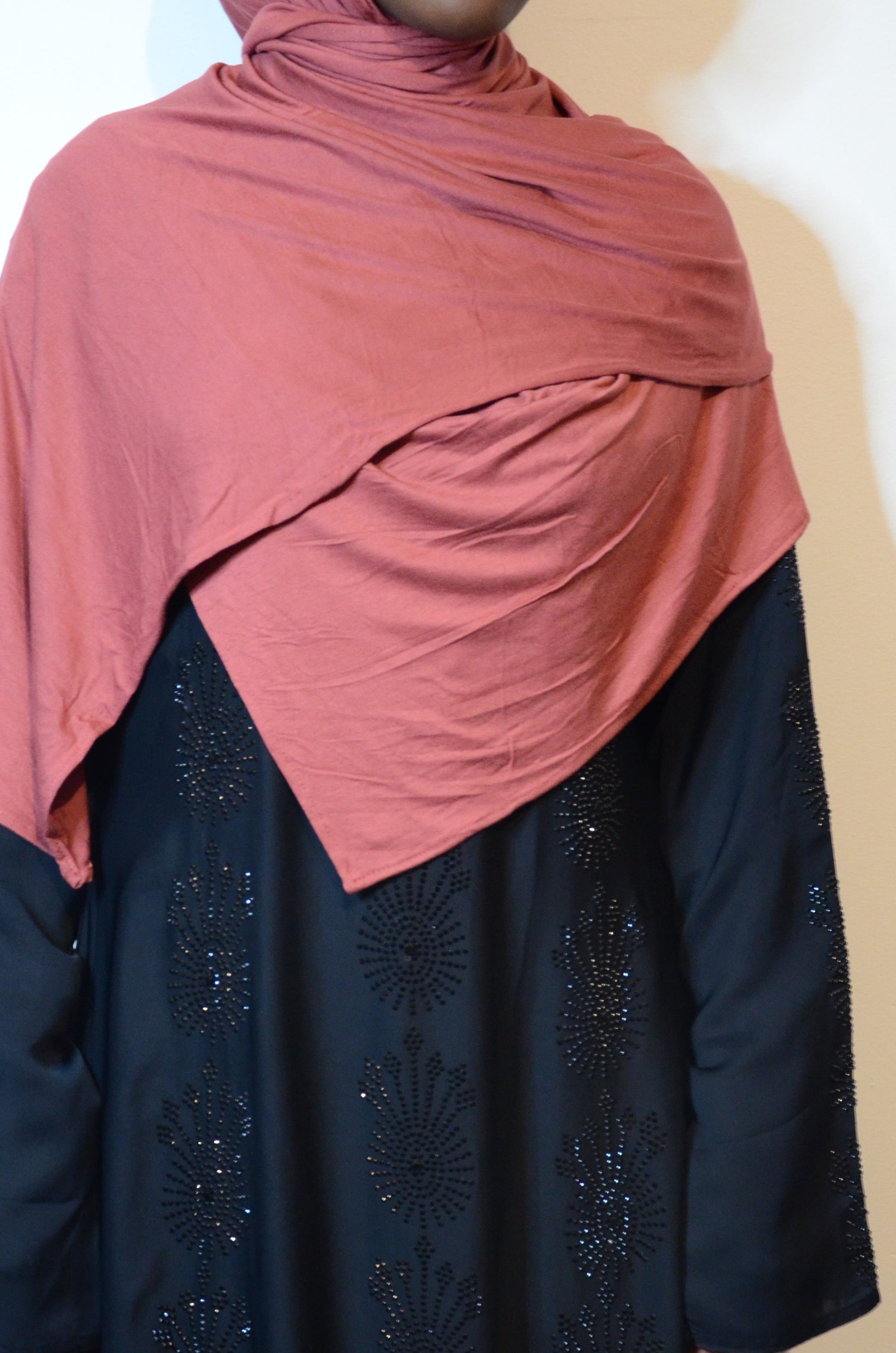 Model wearing a dusty rose plain jersey hijab draped over a black abaya