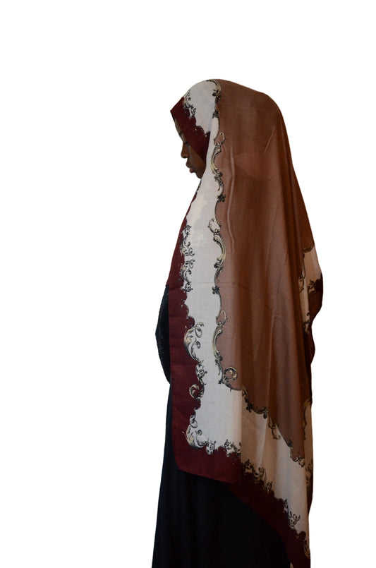 Model wearing a mocha brown cotton voile linen hijab with a burgundy ornate border, styled loosely over a black abaya, side profile.