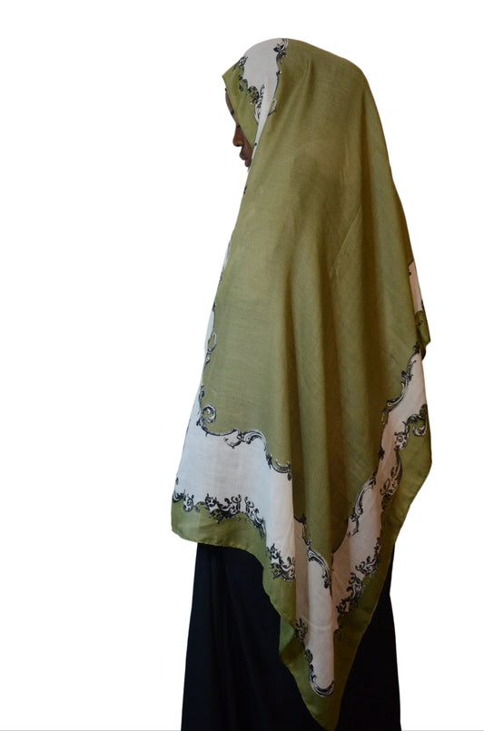 Model wearing an olive green and ivory cotton voile linen hijab with a classic scroll border, side profile view.