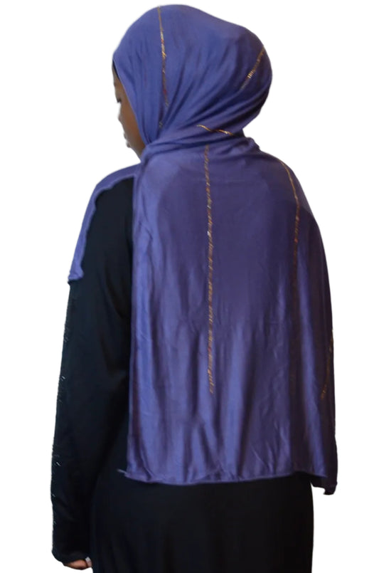 Model wearing a periwinkle blue plain jersey hijab with subtle gold beaded detailing, styled with a black abaya.